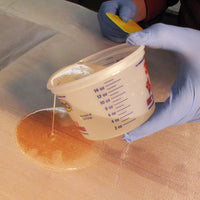 poxy being poured on fiberglass in order to "wet" the weave.