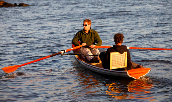 A man rowing an Annapolis Tandem Wherry with a passenger in a cane seat