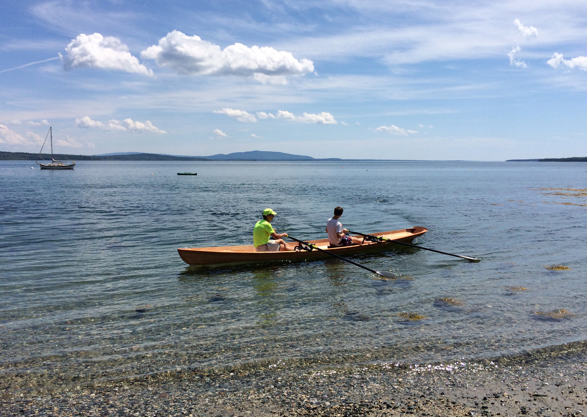 Two men rowing an Annapolis Wherry Tandem built by Bartlett H., near a beach in Brooklin, ME