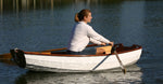 A woman gracefully rows her Eastport Pram in a peaceful harbor. Thumbnail