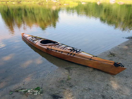 Chris S built this Chesapeake 16 wooden kayak that rests at the water's edge while he is camping in central New Hampshire.