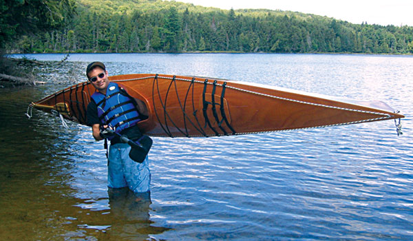 Chris J. carrying his Chesapeake 16 wooden kayak on his shoulder