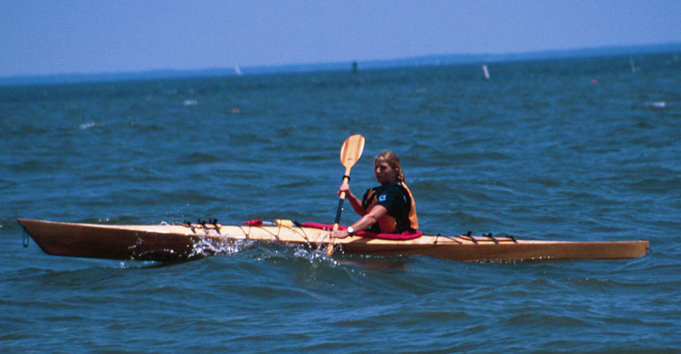 A woman paddling a Chesapeake 16 wooden kayak on the Chesapeake Bay