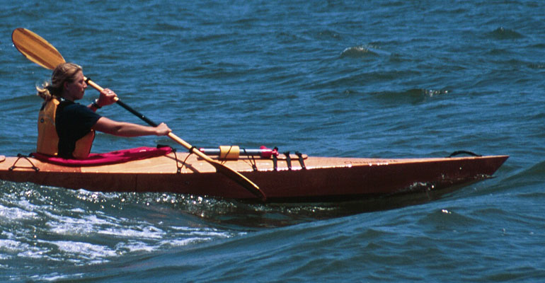 A woman catching a wave in a wooden Chesapeake 16 kayak