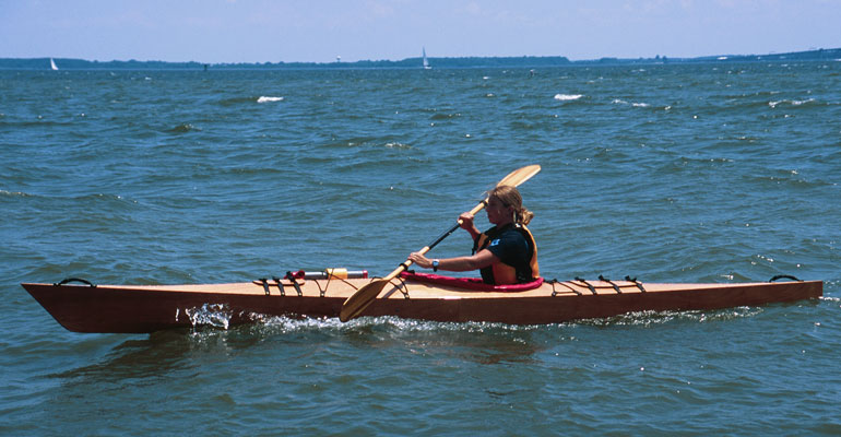 A woman paddling a Chesapeake 16 wooden kayak on the Chesapeake Bay