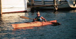 A woman paddling a Chesapeake 1 wooden kayak past a marina Thumbnail