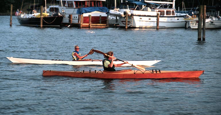 A woman paddling a Chesapeake 16 wooden kayak past a marina