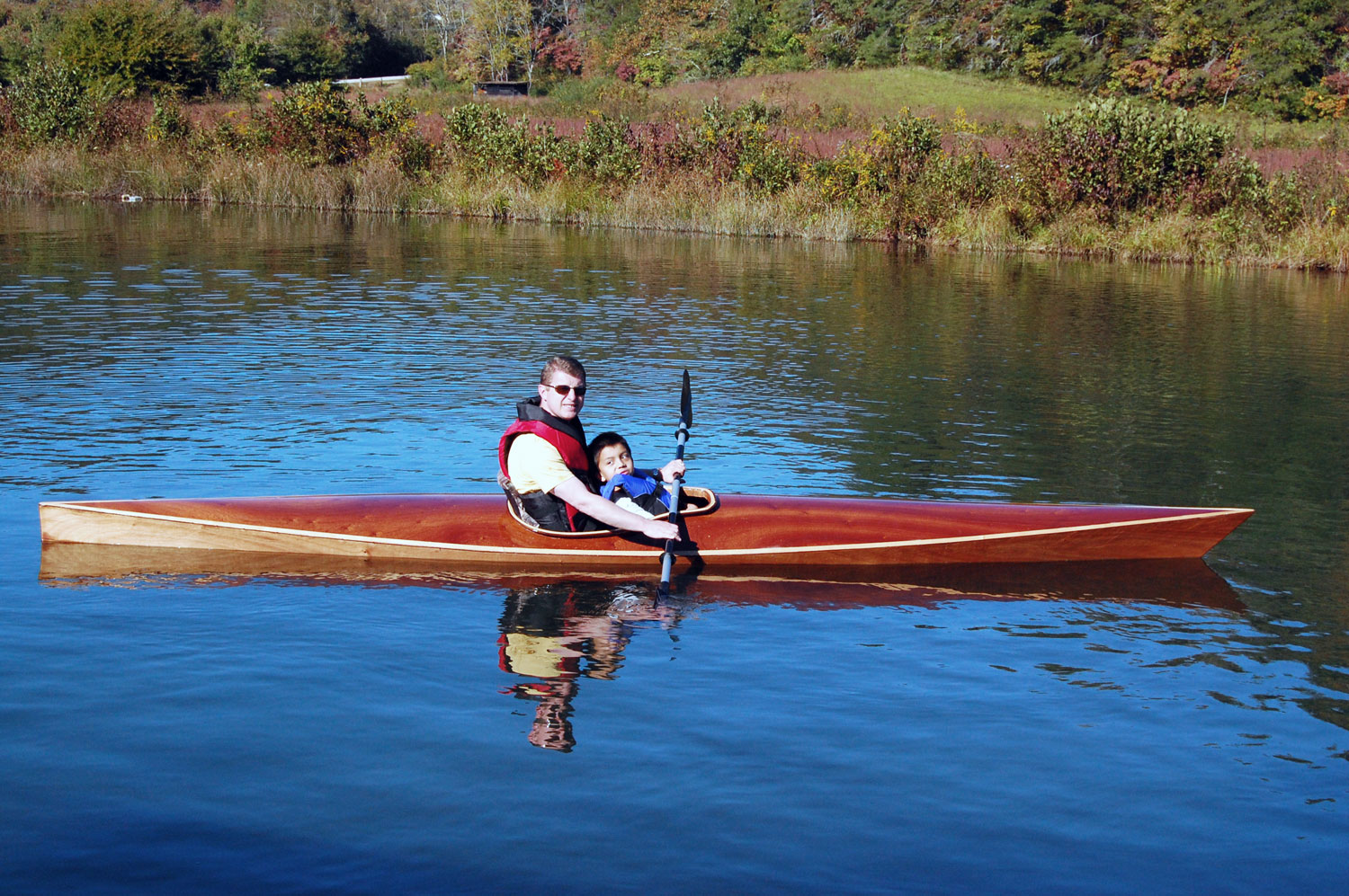 A man and a child enjoying a paddle in a Chesapeake 16 wooden kayak built by Frank J.