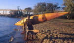 A young man carrying a Chesapeake 16 wooden kayak up onto a beach Thumbnail