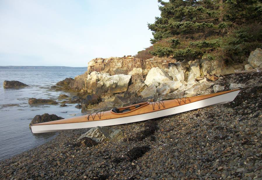 A Chesapeake 16 wooden kayak with white hull, built by David C., on a stony beach