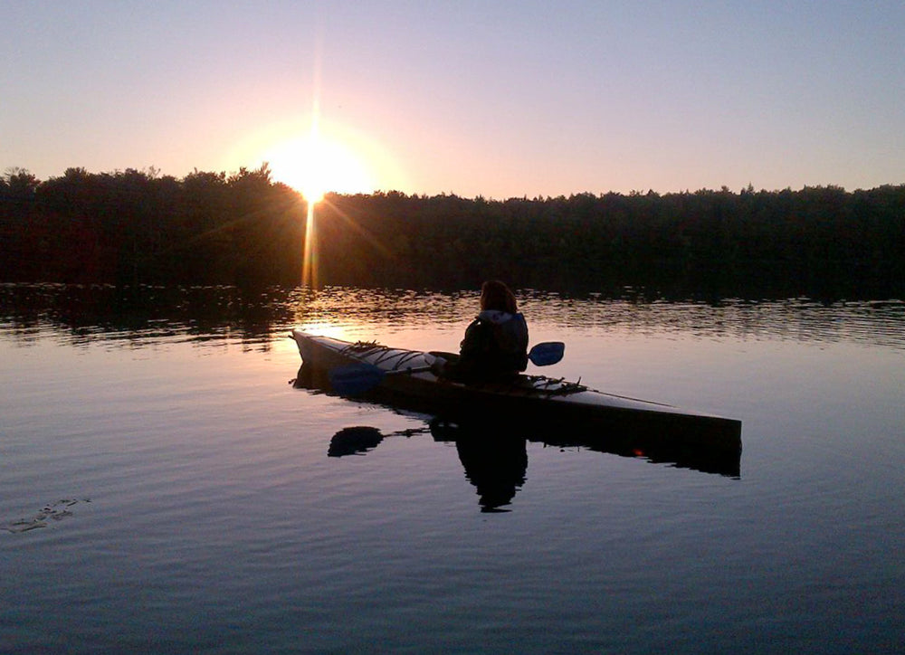 The sun is setting on Dunham Reservoir in Grafton, New York, as Liz B paddles her Chesapeake 16 wooden kayak.