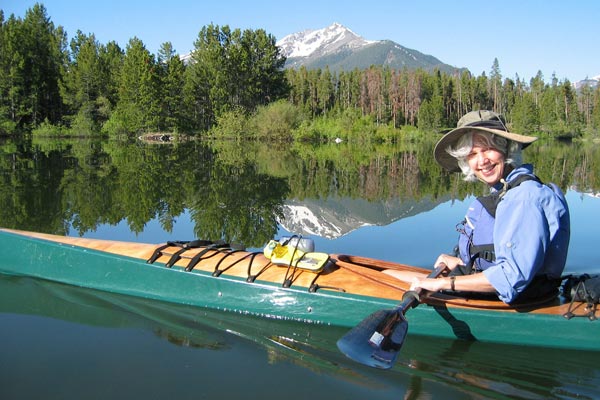 A smiling woman paddling a Chesapeake 17LT wooden kayak on a mountain lake