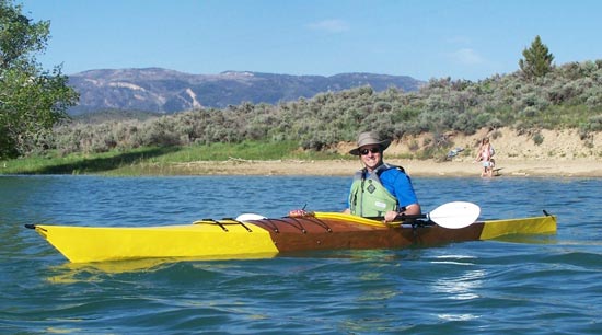 A man paddling a Chesapeake 17LT wooden kayak with striking yellow paint accents