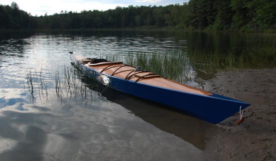 A blue hulled Chesapeake 17LT wooden kayak pulled up among the grasses at the water's edge