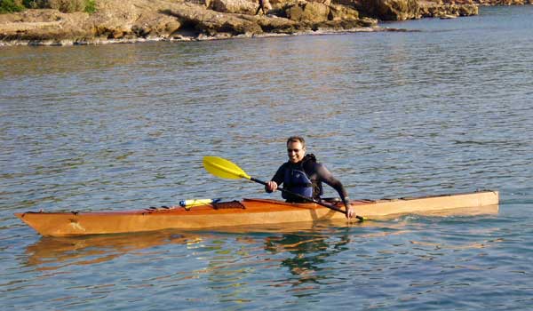 George T. smiling as he paddles his Chesapeake 17LT wooden kayak along a rocky coast
