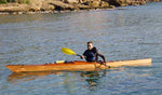 George T. smiling as he paddles his Chesapeake 17LT wooden kayak along a rocky coast Thumbnail