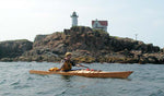 A young paddler passing a lighthouse in a Chesapeake 17LT wooden kayak built by Jon D. Thumbnail