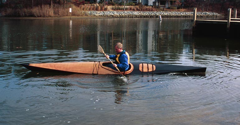 A man bracing a Chesapeake 17LT wooden kayak on a creek