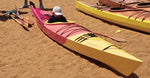 A youngster resting in the cockpit of a beached Chesapeake 17LT wooden kayak with a custom red and yellow paint job Thumbnail