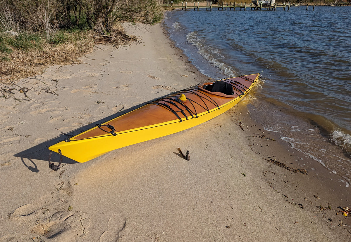 A beached Chesapeake 17LT wooden kayak with yellow hull, built by Dan W., Prince Frederick, MD