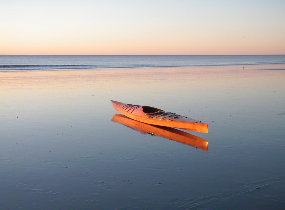 A Chesapeake 17LT wooden kayak built by Frank O.  reflected in the shallows of a tide pool on an ocean beach