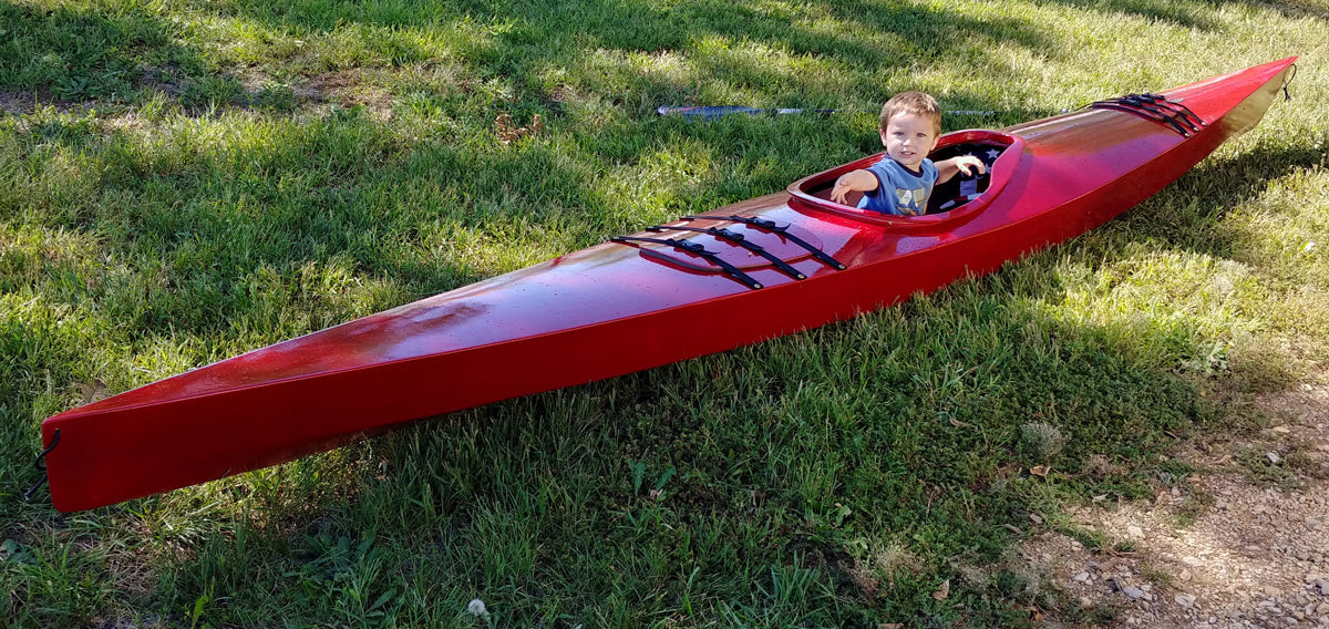 A little boy in the cockpit of a bright red Chesapeake 17LT wooden kayak built by Keith G.