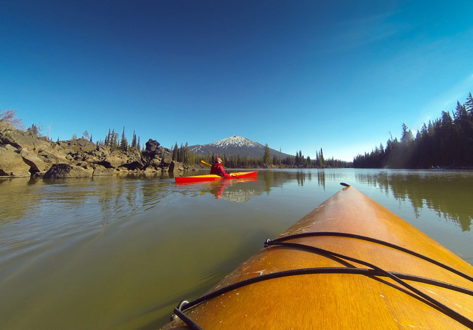 Looking over the bow of a Chesapeake 17LT wooden kayak at another one, framed by a mountain on Sparks Lake, Oregon
