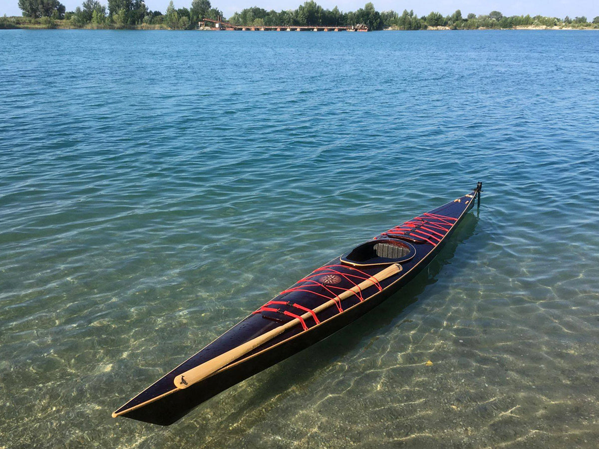 A dark hulled Chesapeake 17LT wooden kayak with bright accents built by Ottoffy Z in Hungary floating on clear water