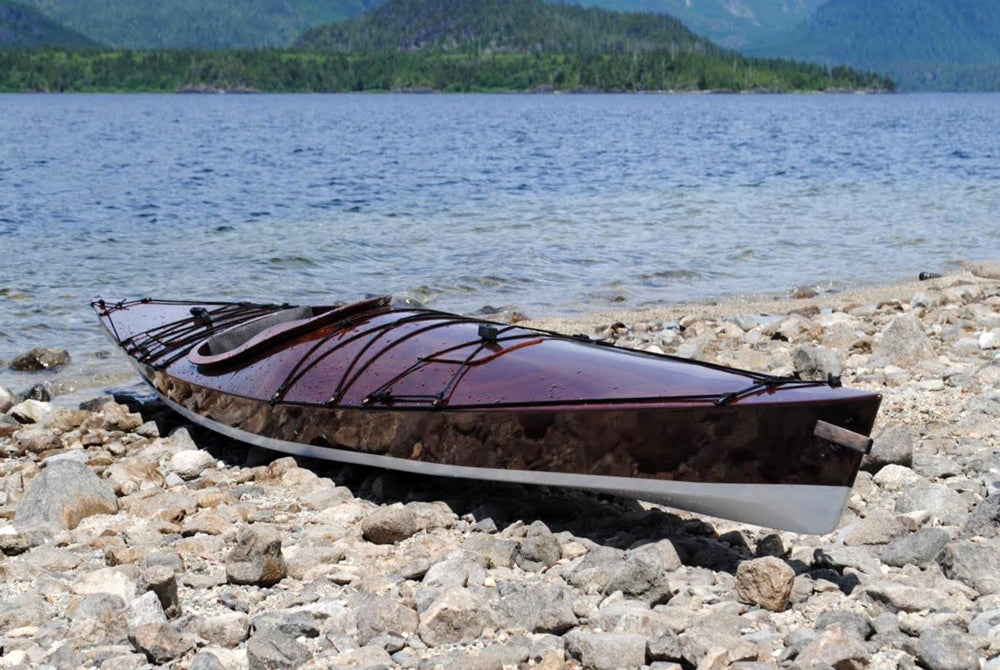 A gleaming dark wood Chesapeake 17LT kayak built by Reade J. on a rocky beach in Victoria, BC