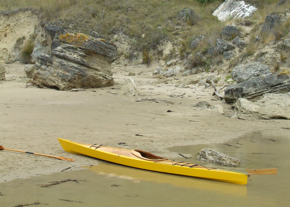 A yellow-hulled Chesapeake 17LT wooden kayak built by Stephen J. pulled up on a beach