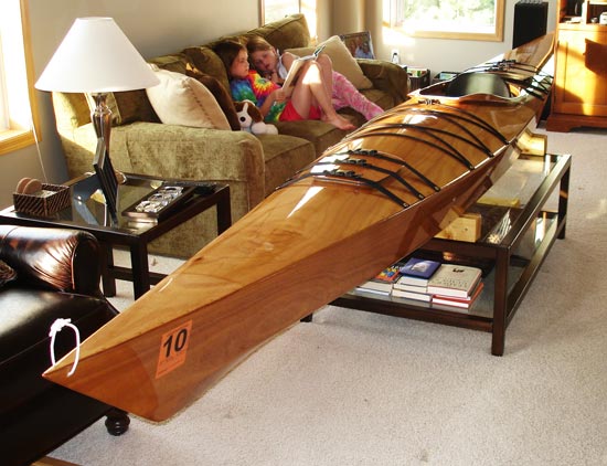 A Chesapeake 17 wooden kayak on a coffee table in a living room with two young girls