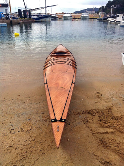 A bow-on view of a Chesapeake 17 wooden kayak built by Johan V. on a beach

