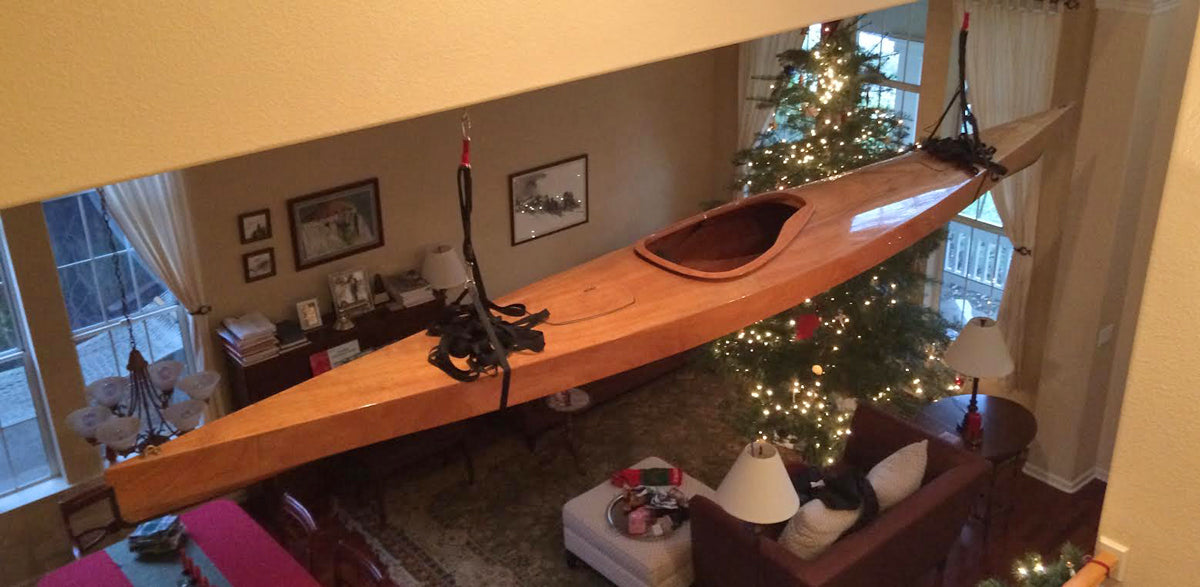 Look what Santa brought: a Chesapeake 17 wooden kayak built by Rick L. suspended from a ceiling in a living room with a Christmas tree
