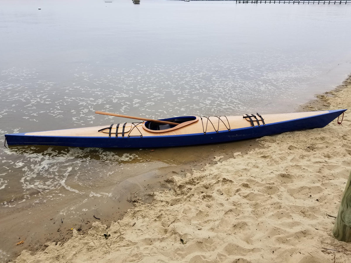 A Chesapeake 17 wooden kayak built by Matt N. at the water's edge on a sandy beach