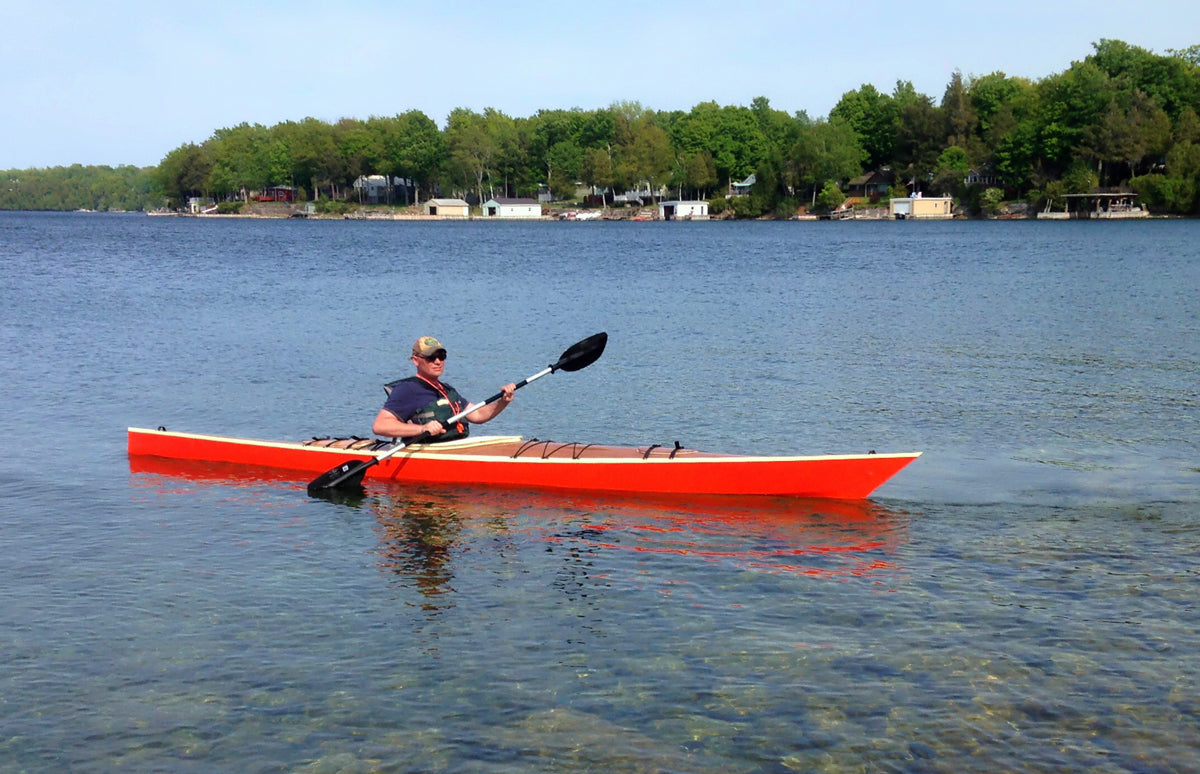 A man paddling a bright red Chesapeake 17 wooden kayak built by Peter A. on the St. Lawrence Rive in Clayton, NY