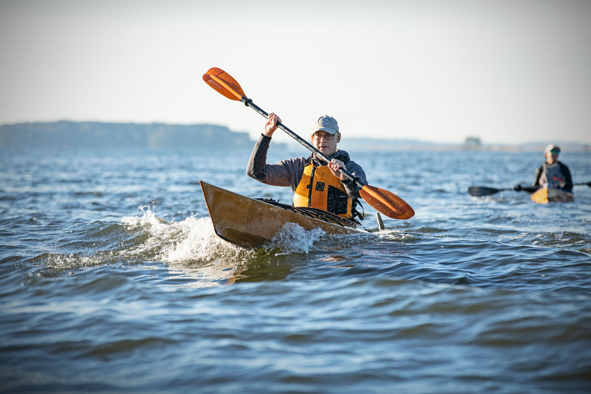 A man paddling a Chesapeake 17 wooden kayak on choppy water