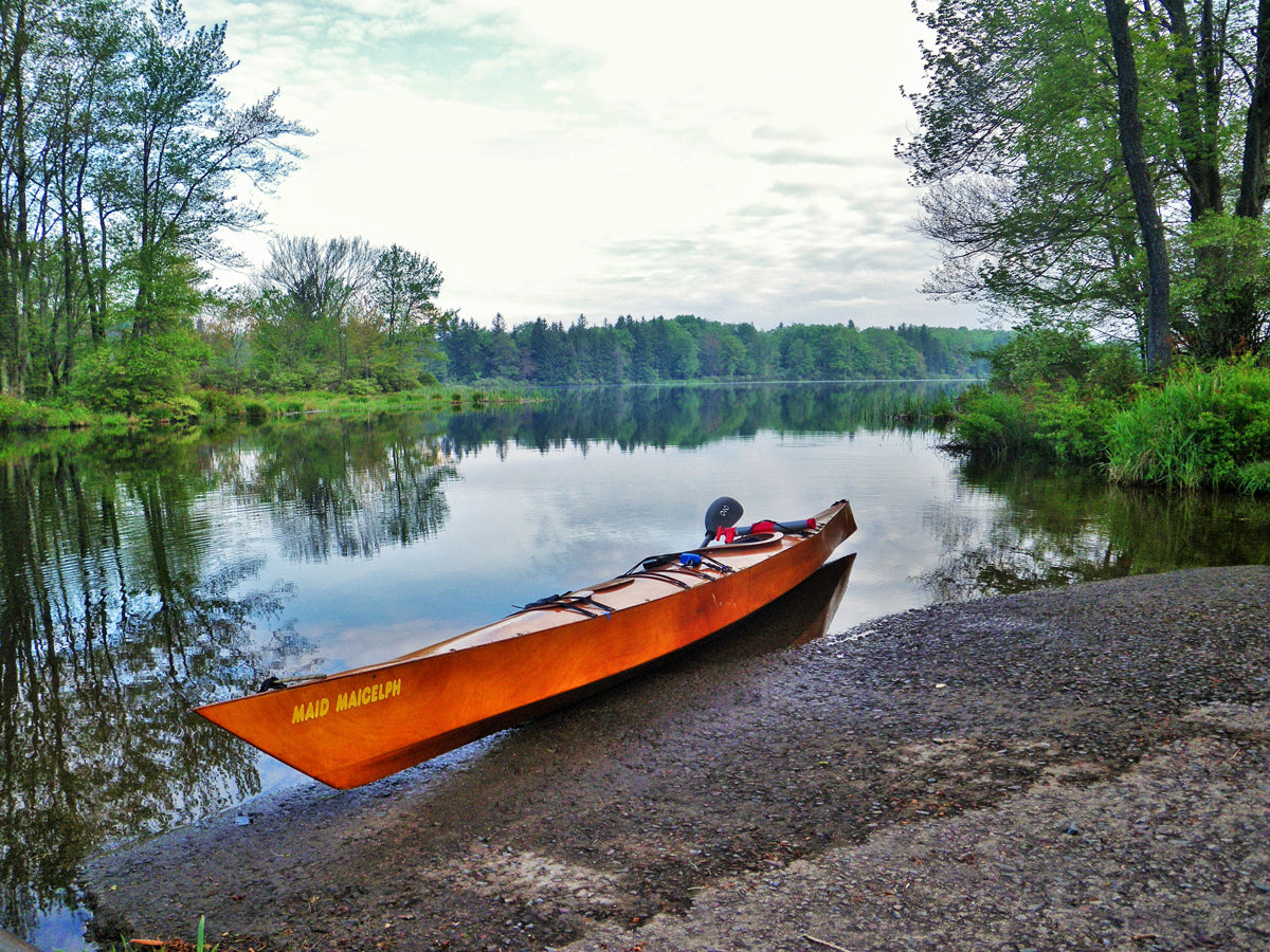A beautifully cared-for 20-year-old Chesapeake 17 wooden kayak built by Andy S pulled up at the edge of a lake