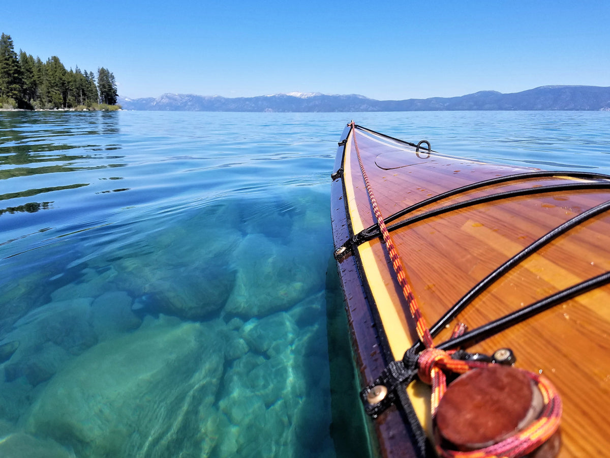 The bow of Mike J's Chesapeake 18 hybrid wooden kayak with a view of the strip-planked deck over the clear water of Lake Tahoe