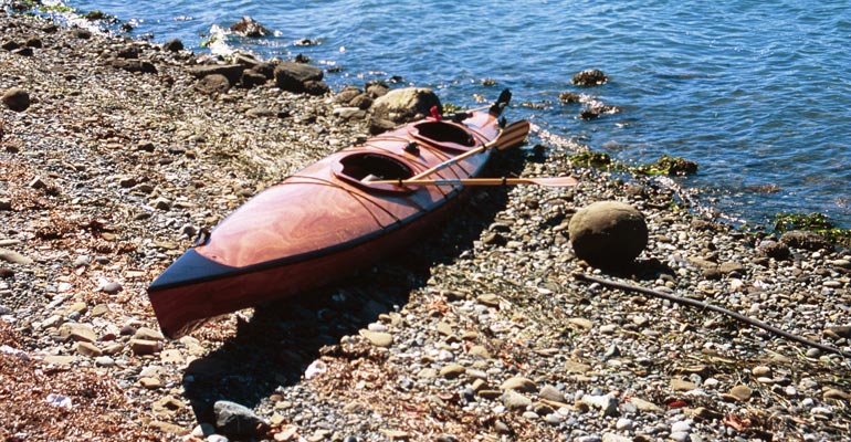 A Chesapeake Double wooden kayak beached on a stony shore