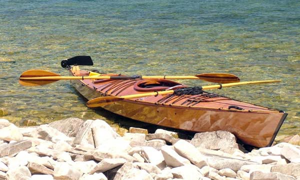 A Chesapeake Double wooden kayak beached on a rocky shore