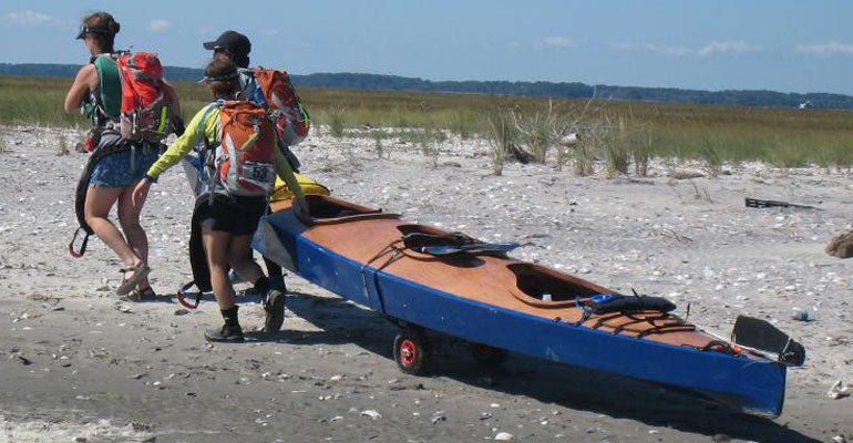 Three paddlers carrying a Chesapeake Triple wooden kayak ashore after a two mile race. Built by Andrew D.
