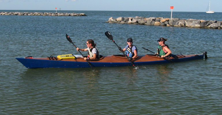 The team of three paddlers heading for the beach in a Chesapeake Triple wooden kayak bulit by Jason R.