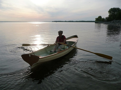 The sun is setting as a woman rows her Chester Yawl on the Ottawa River.
