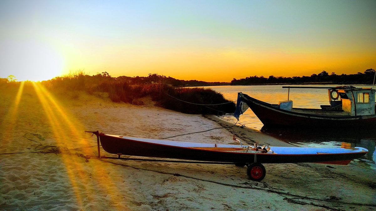 An Expedition Wherry on a trailer in the foreground as the sun dips behind the horizon.