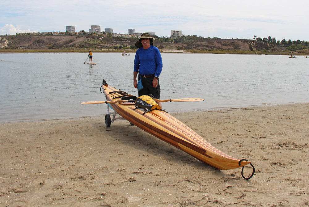 A man showing off his Guillemot Single wooden kayak on the shore at Newport Beach, CA