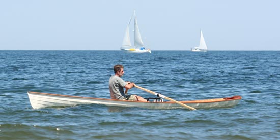 A man rowing an Annapolis Wherry with sailboats in the background