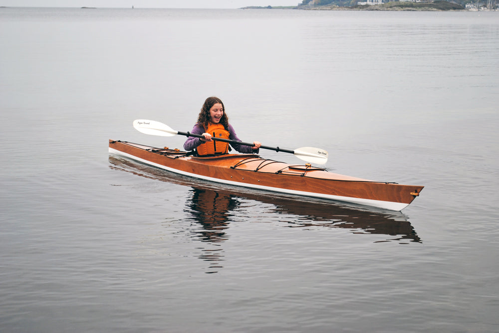 A young girl delights in paddling a Chesapeake 16LT wooden kayak built by Reade J. at Willows Beach near Victoria, BC