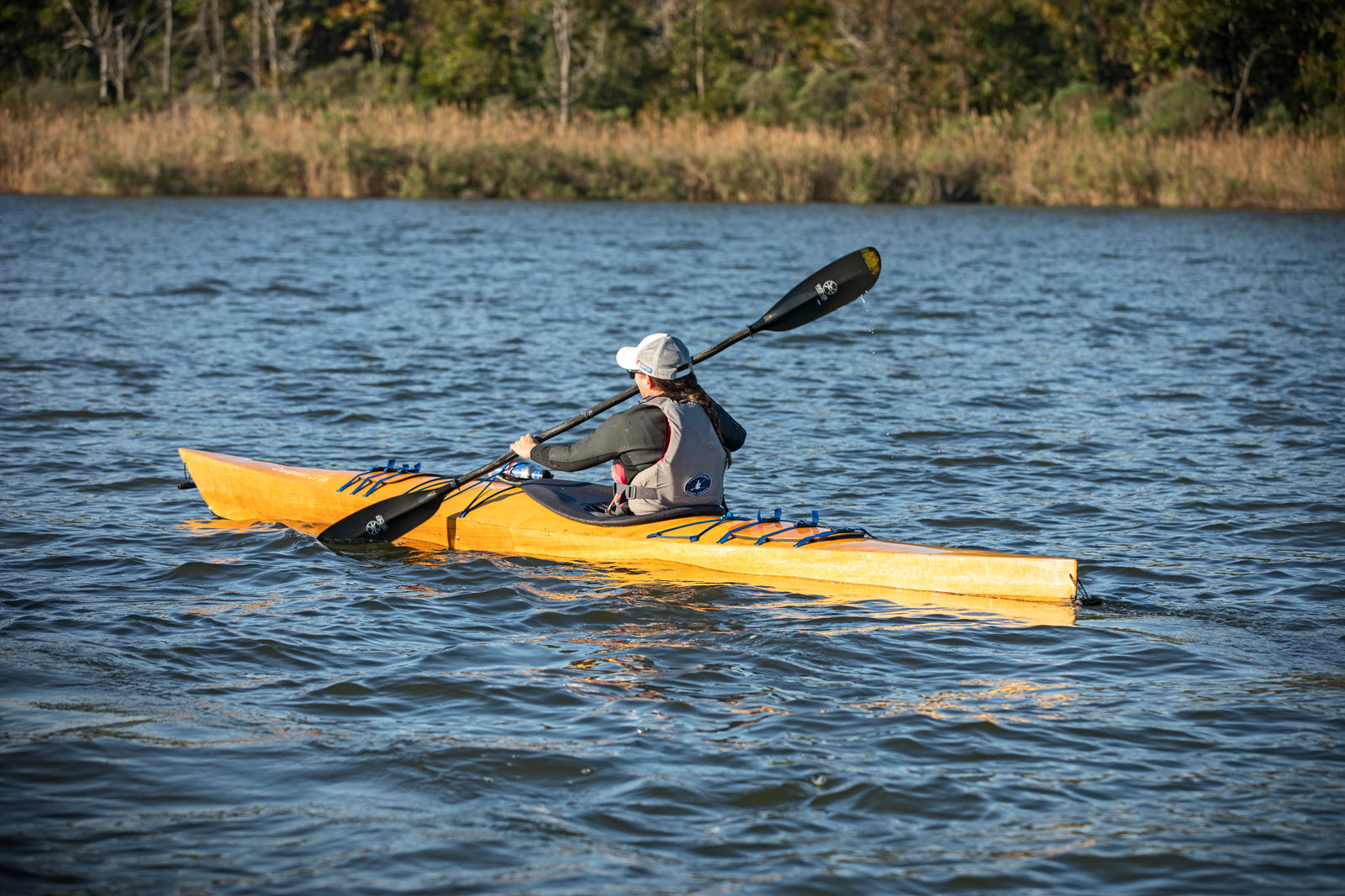 A woman paddling a Chesapeake 16LT wooden kayak along a marshy shore