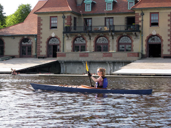 A young woman paddling on the Charles River in Boston in a Chesapeake 14 wooden kayak built by George B.
