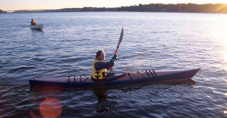 A woman paddling a Chesapeake 14 wooden kayak on the river
